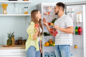 Young couple taking food out of fridge in kitchen�