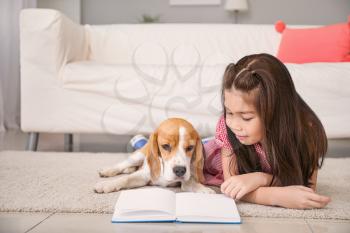 Little Asian girl with cute beagle dog reading book at home�