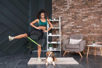 Sporty African-American woman with cute dog training at home�