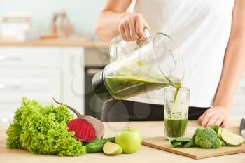 Woman pouring healthy smoothie into glass in kitchen�
