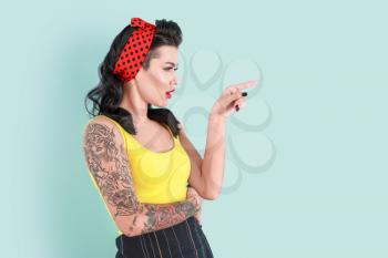 Portrait of beautiful tattooed pin-up woman pointing at something on color background�