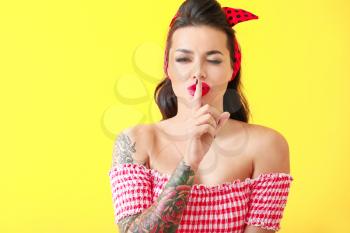 Portrait of beautiful tattooed pin-up woman showing silence gesture on color background�