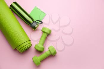 Dumbbells with notebook, yoga mat and bottle of water on color background�