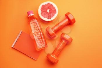 Dumbbells with notebook, grapefruit and bottle of water on color background�