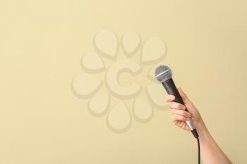 Female hand with microphone on color background�