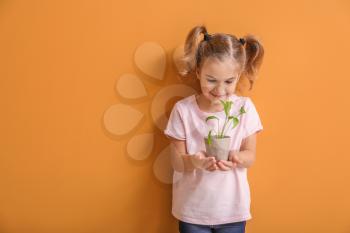 Happy little girl with young plant in pot on color background�
