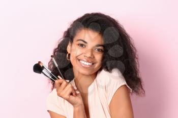 Beautiful African-American woman with makeup brushes on color background�