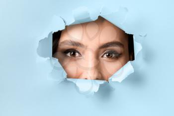 Face of beautiful young woman visible through hole in color paper�