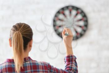 Young woman playing darts indoors�