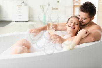 Happy young couple drinking champagne while taking bath together�
