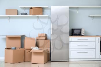Cardboard boxes with belongings and fridge in kitchen of new flat on moving day�