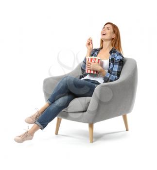 Beautiful woman with popcorn watching TV while sitting in armchair against white background�