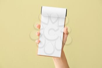 Female hand with blank notebook on color background�