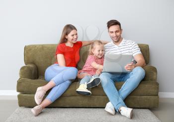 Happy young family with laptop sitting on sofa near light wall�