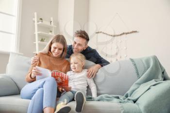 Happy young family reading fashion magazine while sitting on sofa at home�