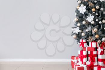 Decorated Christmas tree and gifts near light wall�