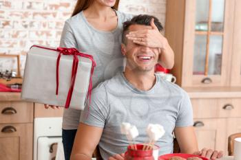Happy young woman giving Christmas present to her boyfriend at home�