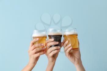 Hands with glasses of beer on color background�