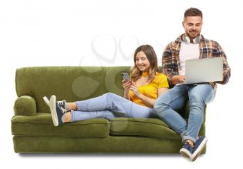 Young couple with laptop and mobile phone sitting on sofa against white background�