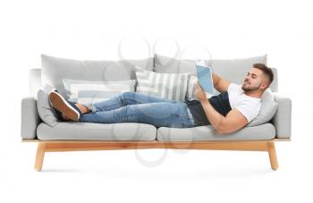Young man with book lying on sofa against white background�