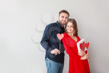 Happy young couple with hearts and gift on light background. Valentine's Day celebration�