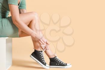 Young woman tying shoelaces against color background�