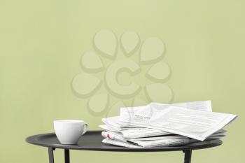 Stack of newspapers and coffee on table against color background�
