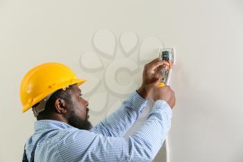 African-American electrician installing switch in room�
