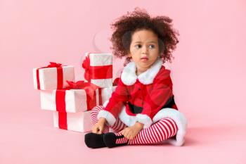 Little African-American girl in Santa costume and with gift boxes on color background�