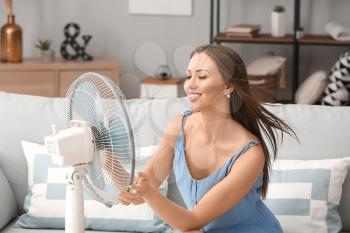 Young woman using electric fan during heatwave at home�