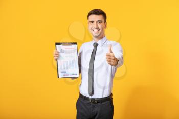 Male bank manager with document showing thumb-up gesture on color background�