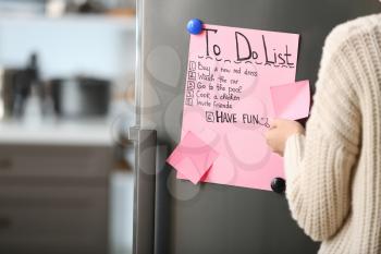 Woman checking to-do list on fridge in kitchen�
