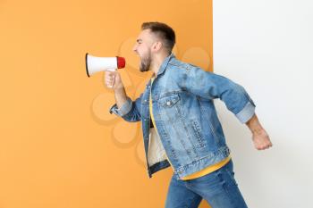 Emotional young man with megaphone on color background�