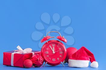 Alarm clock with Christmas gift and Santa Claus hat on color background�