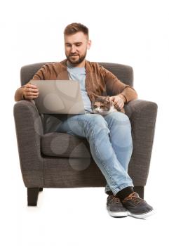 Man with cute cat and laptop sitting in armchair on white background�