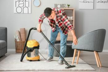 Young Asian man hoovering floor at home�
