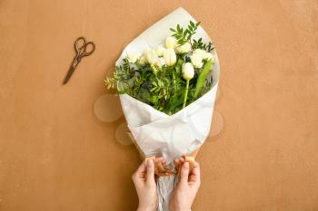 Female florist making beautiful bouquet on color background�