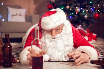 Funny drunk Santa Claus stretching hand for beer while lying on floor�