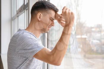 Depressed young man near window�