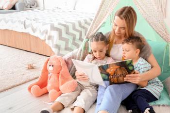 Nanny and cute little children reading book at home�