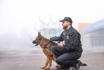 Male police officer with dog patrolling city street�