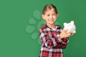 Cute girl with piggy bank on color background�