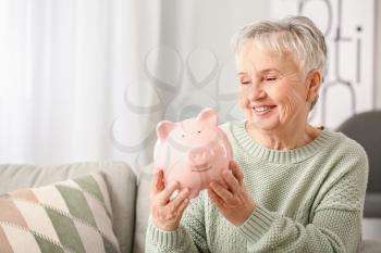 Senior woman with piggy bank at home�