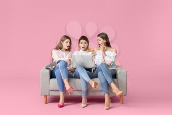 Surprised young women with laptop sitting on sofa against color background. Online shopping concept�