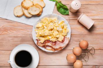 Plate with scrambled egg and bacon on table�
