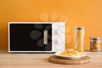 Plate with tasty pasta and microwave oven in kitchen�