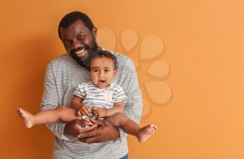 Happy African-American man with cute baby on color background�