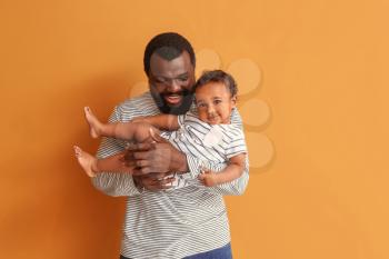 Happy African-American man with cute baby on color background�