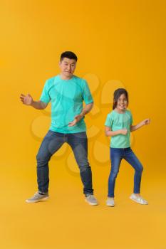 Happy Asian man dancing with his little daughter on color background�