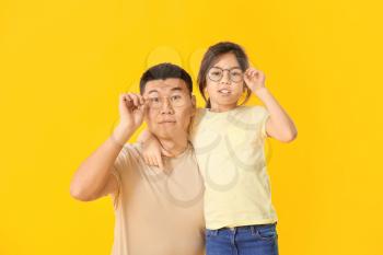 Asian man and his little daughter wearing glasses on color background�